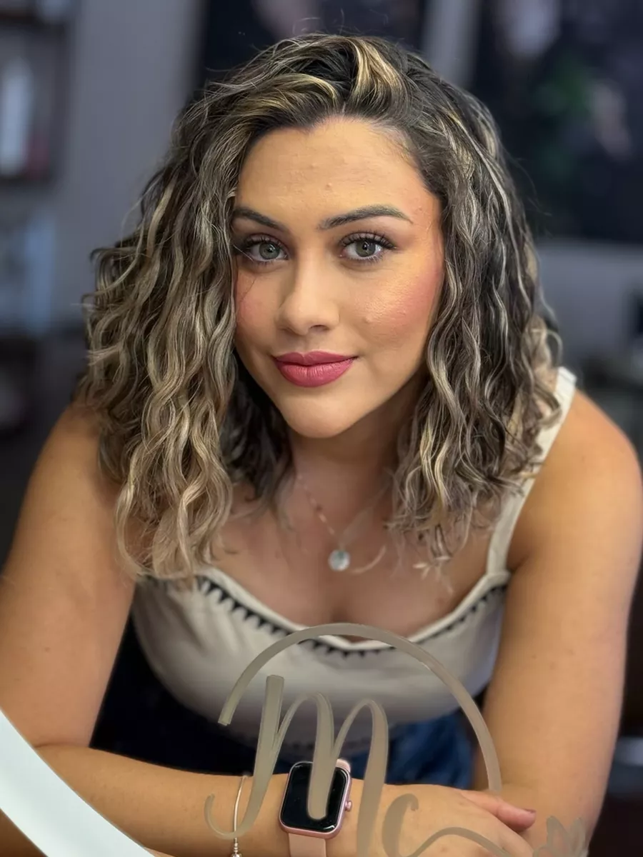 Cliente com cabelo cacheado médio e luzes douradas, diante do espelho com a logo do studio