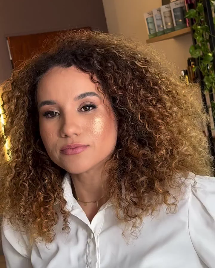 Mayra Cristh, cabeleireira e colorista, de blusa branca e cabelo cacheado